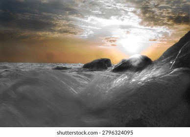 Dynamic low angle shot of a powerful ocean wave crashing against coastal rocks during a golden sunset, featuring artistic high contrast and moody atmosphere