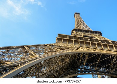 Dynamic low angle view of the Eiffel Tower against blue sky.