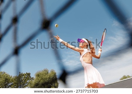 Dynamic low angle view of female tennis player tossing ball before serve on outdoor court. Ideal for sports advertising, tournament promotion, and performance campaigns.