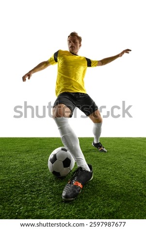 Dynamic low angle view of young man, soccer player controlling ball, stabilizing stance, preparing for next move during match and training session against white background. Concept of game, sport