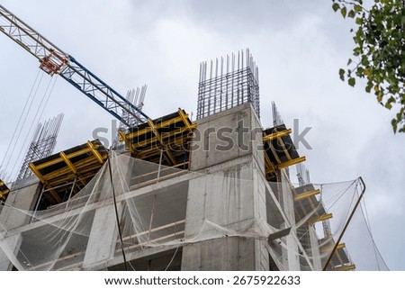 Dynamic low-angle perspective of multi-story building under construction, featuring raw concrete, exposed rebar, temporary yellow formwork, protective safety nets, and prominent tower crane against ov