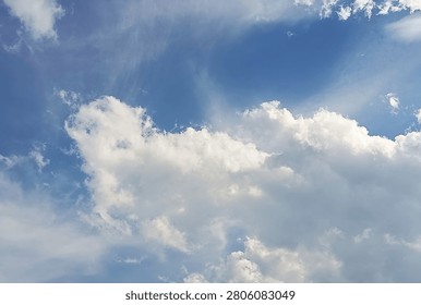A dynamic low-angle shot of a bright blue sky filled with large, fluffy white cumulus clouds, featuring delicate wispy cirrus textures across the frame