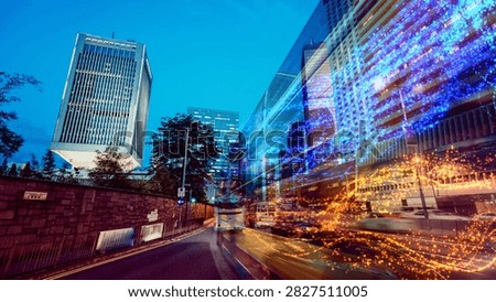 A dynamic, low-angle shot captures the dazzling energy of Hong Kong's urban landscape, featuring towering glass buildings illuminated with streaks of colorful light against the deep blue evening sky