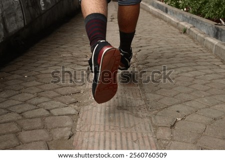 A dynamic low-angle shot capturing the motion of a person walking along a cobblestone pathway. The focus is on the sole of the shoe mid-stride, showcasing its detail, while the striped socks.