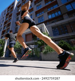 Dynamic low-angle shot of two runners in a city, focusing on the woman's brightly colored sneakers and muscular legs. Concept of sport and healthy lifestyle, pair training, motion, activity.