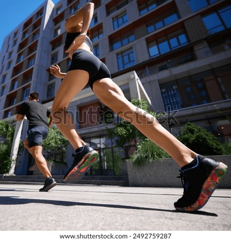 Dynamic low-angle shot of two runners in a city, focusing on the woman's brightly colored sneakers and muscular legs. Concept of sport and healthy lifestyle, pair training, motion, activity.