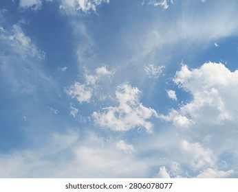 A dynamic low-angle shot of a vibrant blue sky filled with scattered white cumulus clouds mixed with soft, sweeping wispy cloud textures