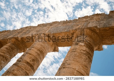 Dynamic low-angle view of Doric columns and architrave against blue sky with clouds in Segesta, Sicily, Italy