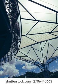 A dynamic, low-angle view showcasing modern tensile fabric architecture against a vibrant blue sky with scattered clouds.