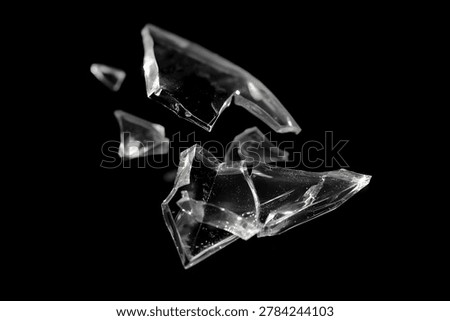Dynamic macro image of sharp transparent glass fragments exploding and suspended in mid-air against a high-contrast black background.