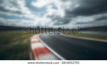 A dynamic, motion-blurred view of a racing circuits asphalt track with distinctive red and white curbs, set against a dramatic, overcast sky.