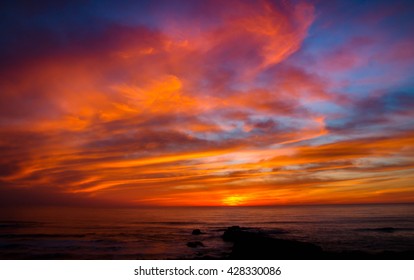 Dynamic ocean sunset from Pescadero State Bean along Highway One in central California.  Red, Orange and yellow reflect in the quick moving clouds. - Powered by Shutterstock