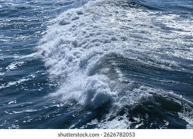 Dynamic ocean wave featuring foam and ripples illuminated by sunlight, showcasing natural seaside energy. Background photo texture
