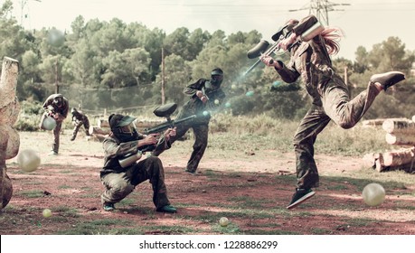 Dynamic paintball battle. Portrait female player jumping and aiming marker on player of opposing team