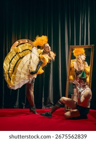 Dynamic performance with two cabaret actors in eccentric vintage outfits pose on red carpet with confetti. Man and woman in eccentric scene. Concept of cabaret, show, circus, retro, vintage