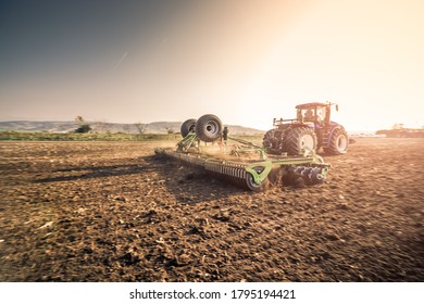 Dynamic photo of big blue modern tractor during stubble-tillage cultivation after harvest for maximum  fertility of soil and the field. Sunny morning photo with flare from the sun.