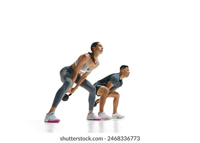 Dynamic photo of young man and woman shown exercising with kettlebells in squat position against white studio background. Concept of people in sport, healthy lifestyle, teamwork, motivation. Ad - Powered by Shutterstock