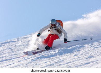 Dynamic picture of a skier on the piste in Alps. Woman skier in the soft snow. Active winter holidays, skiing downhill in sunny day. Ski rides on the track with swirls of fresh snow.