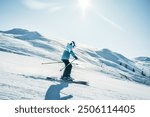 Dynamic picture of woman skier in blue outfit on the piste ski downhill fast motion in Alps. Active winter holidays, skiing downhill in overcast day. Ski rides on the track with swirls of fresh snow