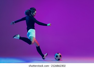 Dynamic portrait of female soccer player practicing with football ball isolated on purple studio background in neon light. Concept of sport, action, motion, fitness. Young spotive girl training - Powered by Shutterstock
