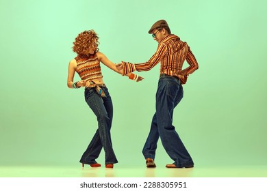 Dynamic portrait of happy man and woman in retro colored shirts and flared jeans dancing energetic dance over green background. Concept of fashion trends of 70s, 1980s years, music, hippie lifestyle - Shutterstock ID 2288305951