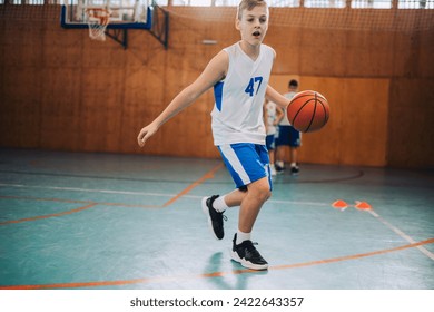 Dynamic portrait of a junior basketball player in action practicing and dribbling a ball on training at indoor court. A young athlete is practicing basketball and learning moves on training.Copy space - Powered by Shutterstock