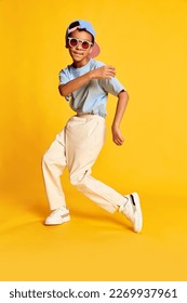 Dynamic portrait of little african boy, hip-hop dancer in stylish street style clothes dancing over bright yellow background. Concept of music, dance happiness. Kid looks happy and sportive - Shutterstock ID 2269937961