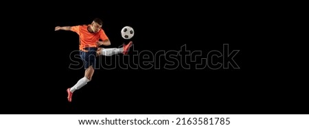 Dynamic portrait of professional male football soccer player in motion isolated on dark background. Concept of sport, goals, competition, hobby, ad. Sportsmen wearing orange-blue football kit