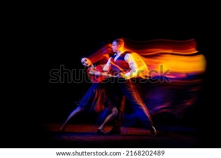 Dynamic portrait of young ballroom dancers dancing Argentine tango isolated on dark background with neon mixed light. Concept of art, beauty, grace, action, emotions. Copy space for ad