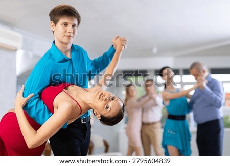 In dynamic salsa dance class, positive young couple in elegant attire skillfully performing dip move, adding touch of elegance and passion to routine..
