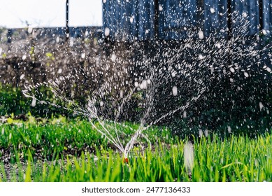 Dynamic shot capturing action of water sprinkler irrigation lush green lawn. Water droplets are caught in mid-air, creating a beautiful pattern against backdrop of garden.