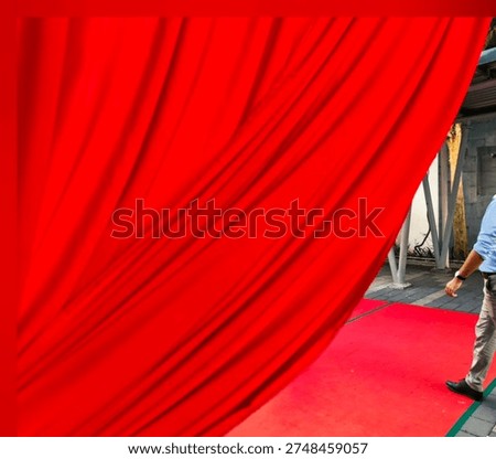 Dynamic shot capturing the moment a vibrant red curtain is pulled back, revealing a person walking along a matching red carpet. This image evokes feelings of exclusivity, grand openings, premieres, and VIP events. Ideal for use in marketing materials, event promotions, or any design project requiring a touch of luxury and anticipation.