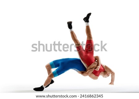 Dynamic shot of two professional Greco-Roman wrestlers in red and blue uniform wrestling against white studio background. Concept of motion, action, combat sports, strength and power, movement,