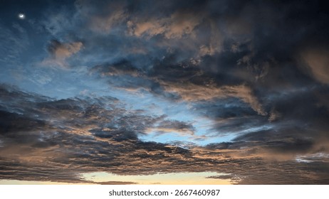 A dynamic sky with a crescent moon in the upper left corner. Layers of textured clouds in dark gray and blue are tinged with warm orange and pink hues, creating a dramatic and colorful scene.