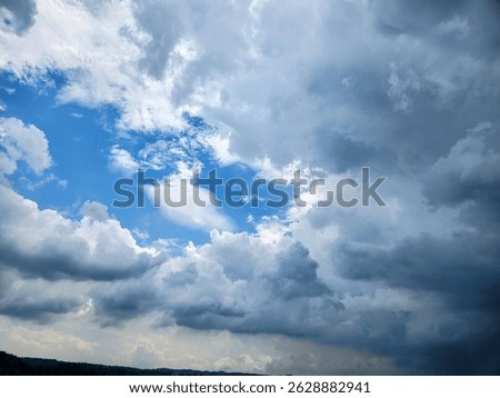 A dynamic sky filled with dramatic storm clouds and patches of blue, showing a weather transition over a distant treeline. A perfect visual for nature, weather, and background themes.