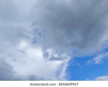 A dynamic sky scene featuring a mix of heavy gray clouds and patches of clear blue sky. The left side of the frame is dominated by dense, textured gray clouds, while the right side opens up to reveal a bright blue background. This contrast highlights a changing weather pattern, typical of a partially cloudy day.