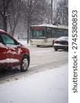 A dynamic street-level shot documents active winter traffic conditions in Bucharest, Romania during a heavy snowstorm, with trolleybus line 70 serving the Bd. Basarabia via Universitate route as the central subject. The cream and grey articulated trolleybus is captured head-on in the middle of the frame, its orange LED destination display clearly readable showing "70 BD. BASARABIA VIA UNIVERSITATE," and its headlights glowing through the curtain of falling snow. The trolleybus overhead collection arms are visible reaching up to the electric wire infrastructure above. A red SUV in the immediate left foreground is captured in motion blur, conveying the active flow of traffic navigating the treacherous snow-covered road surface. A dark sedan occupies the right lane beside the trolleybus. The road surface is a mix of compacted snow, slush, and exposed wet asphalt, with tram rail tracks visible cutting through the white surface. Snowflakes are densely visible mid-air throughout the entire frame, frozen by the camera