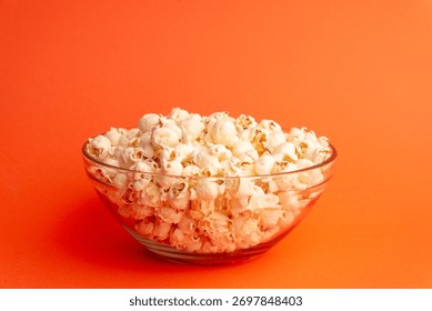 Dynamic studio image with popcorn falling above a glass bowl on orange background, symbolizing fun, motion, and joyful snack moments