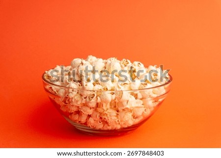 Dynamic studio image with popcorn falling above a glass bowl on orange background, symbolizing fun, motion, and joyful snack moments