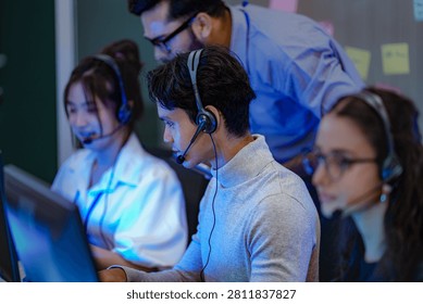A dynamic team of tech support agents wearing headsets and operating desktop computers while a supervisor monitors network performance logs behind them.