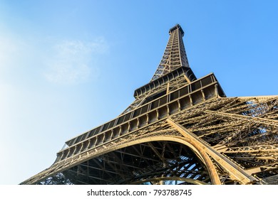 Dynamic view from below of the Eiffel Tower against blue sky.