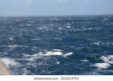 A dynamic view of the ocean with strong waves and choppy waters under a partly cloudy blue sky, showing the intensity of open sea conditions.