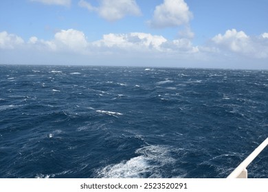 A dynamic view of the ocean with strong waves and choppy waters under a partly cloudy blue sky, showing the intensity of open sea conditions. Seascape marine view nature outdoor