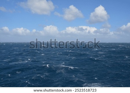 A dynamic view of the ocean with strong waves and choppy waters under a partly cloudy blue sky, showing the intensity of open sea conditions. Nature outdoor landscape seascape photo