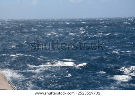 A dynamic view of the ocean with strong waves and choppy waters under a partly cloudy blue sky, showing the intensity of open sea conditions.