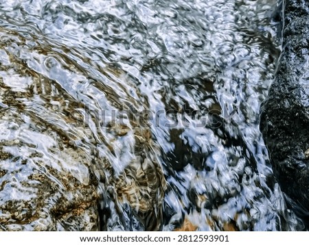 A dynamic view of a small cascade flowing over smooth rocks. The water creates patterns as it hits the stones, showcasing the refreshing and wild nature of the creek.