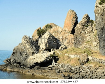 Dynamic volcanic rock formations and unique giant rocks along the coast under a clear sky in Japan.