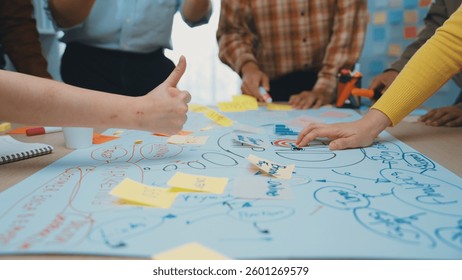 A dynamic workshop scene showcasing multiple hands engaged in writing and planning on a large paper with sticky notes, highlighting teamwork and creative thinking. SACTR
