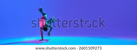 Dynamic young guy, dancer executing powerful breakdance move, blending skill and rhythm against neon blue purple backdrop. Concept of hip-hop culture, movement, artistic expression and youthful energy