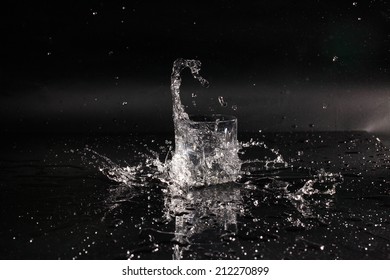 Dynamics Of A Liquid, Glass With Splashed Out Water On A Dark Surface Of A Table